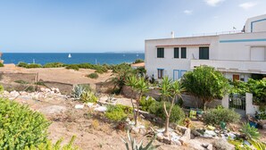 Une propriété située sur la côte, offrant une vue sur la mer, avec un jardin planté de différentes espèces et un bâtiment blanc agrémenté de touches de bleu.