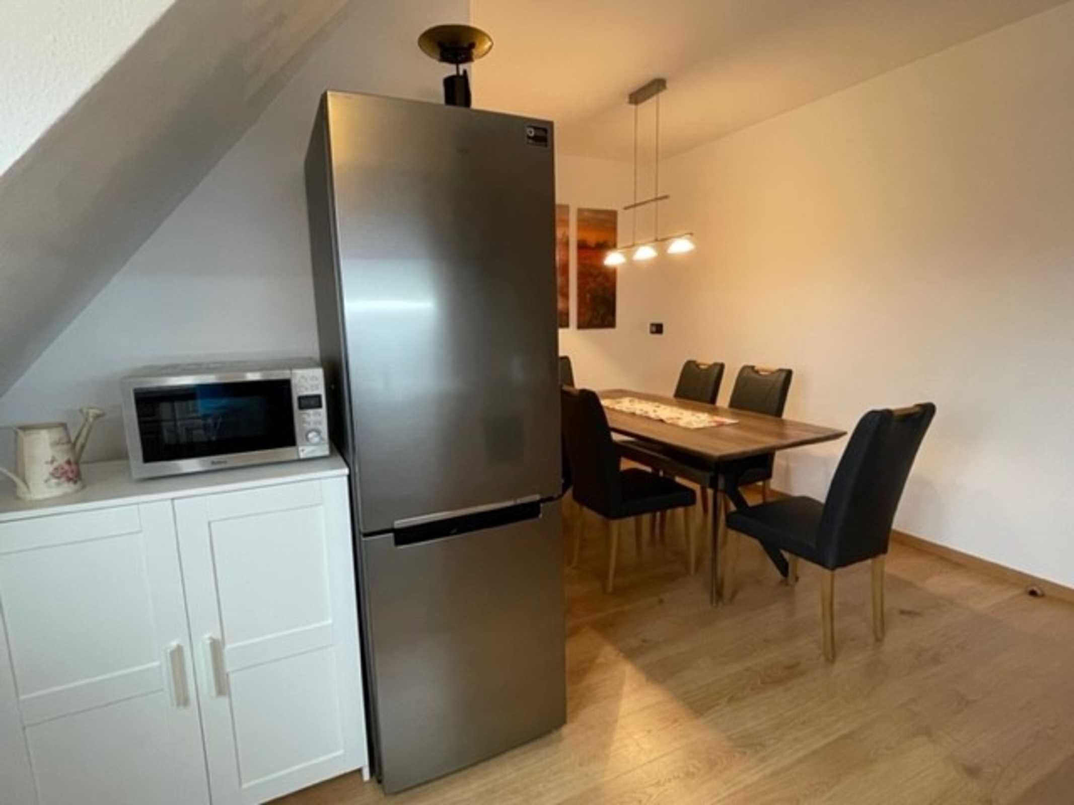 Une cuisine compacte équipée d’un réfrigérateur en acier inoxydable, d’un four à micro-ondes et d’une table à manger avec des chaises.