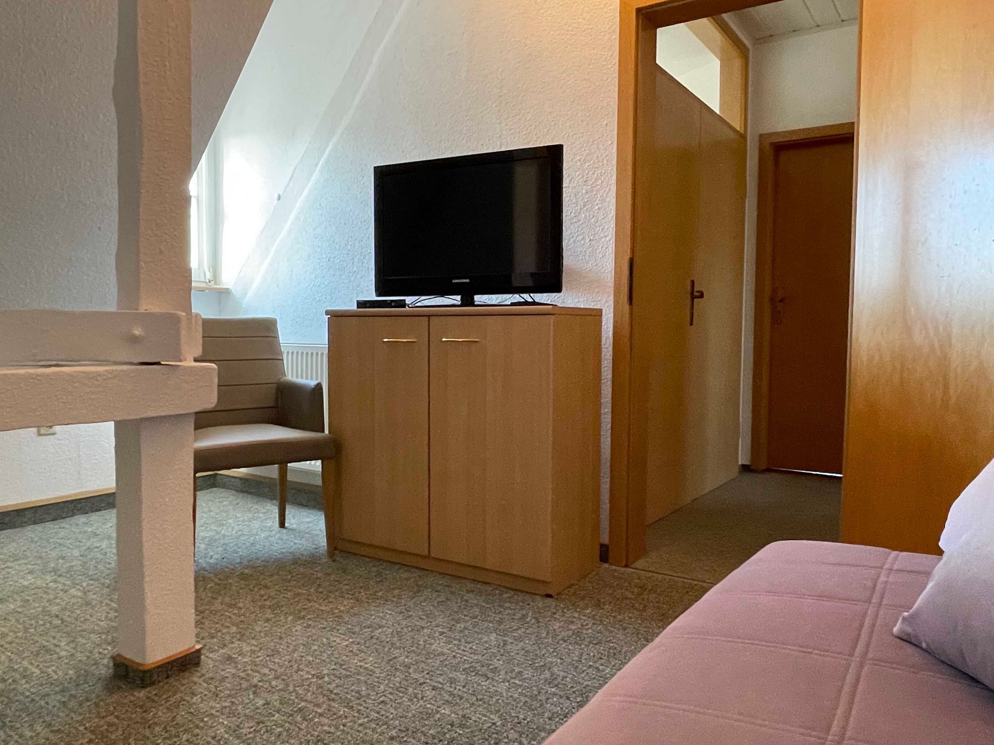A bedroom with a bed, a wooden wardrobe, and a television on top.