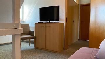 A bedroom with a bed, a wooden wardrobe, and a television on top.