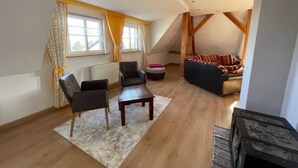 Una sala de estar acogedora de estilo loft, con techo inclinado, vigas de madera, un sofá, dos sillones y una mesa de centro.