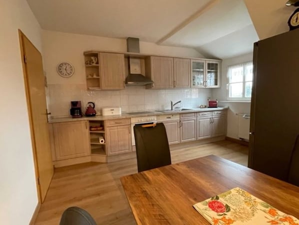 A compact kitchen with light wood cabinets, a built-in oven, and a window providing natural light.