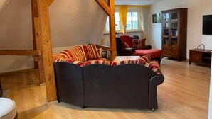 Una sala de estar estilo loft con vigas de madera a la vista, un sofá modular, un sillón rojo y un mueble de madera.