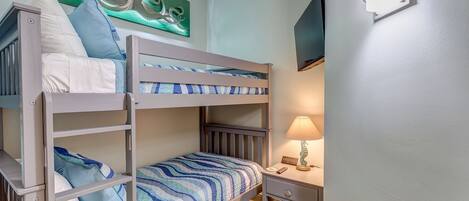 Une chambre avec un lit superposé, une table de chevet et une lampe, un tableau au mur et un luminaire au plafond.