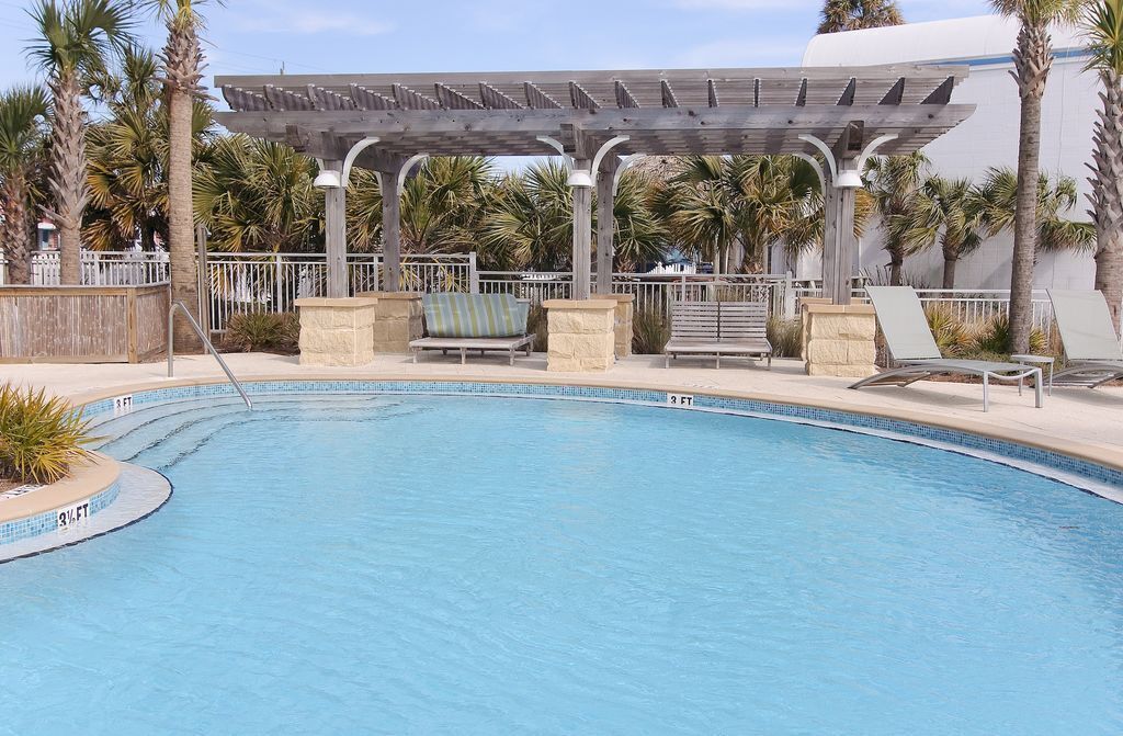 Une piscine avec des chaises longues et une pergola.