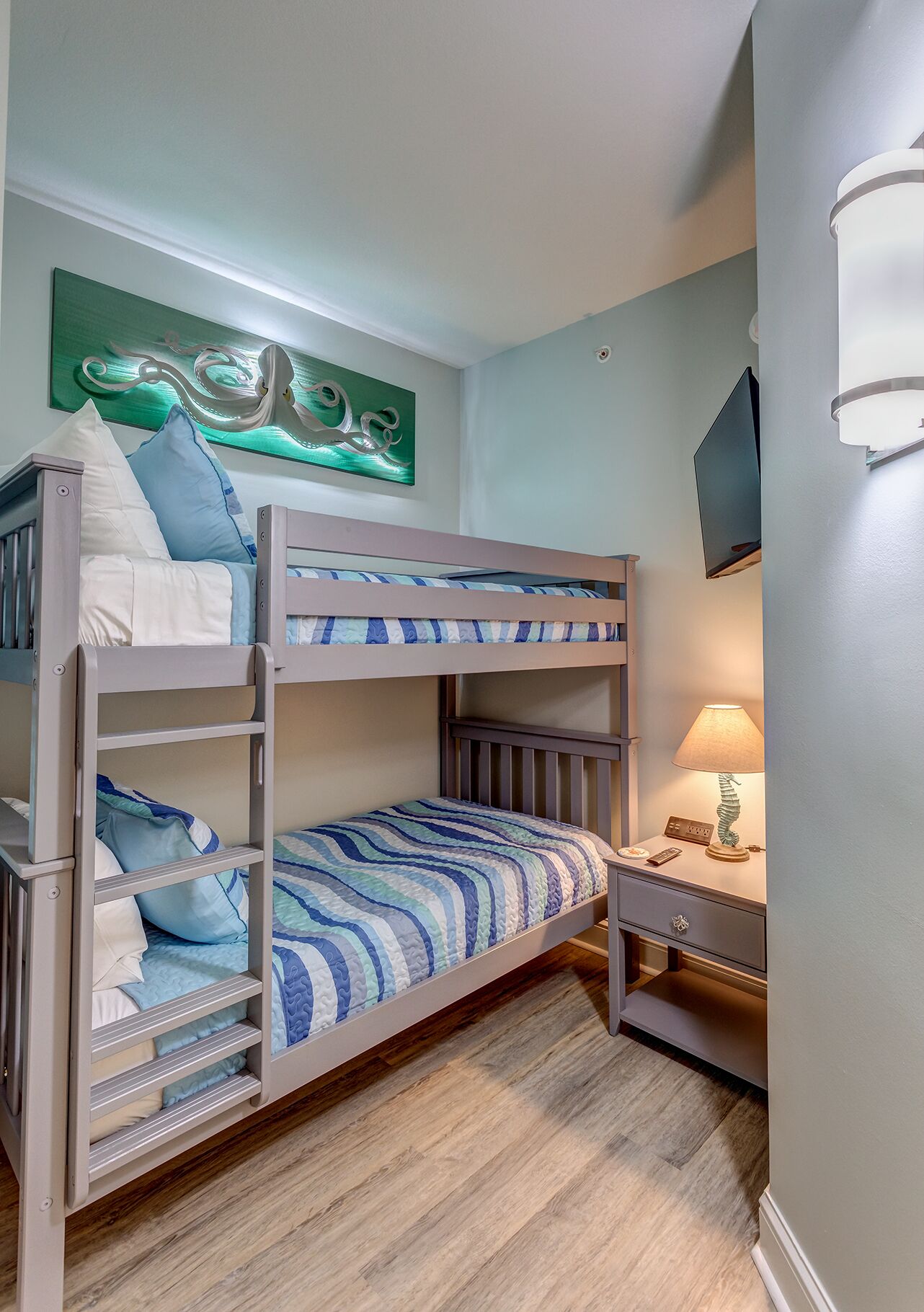 Habitación con literas, un escritorio y una lámpara, un cuadro en la pared y un televisor fijado a la pared.