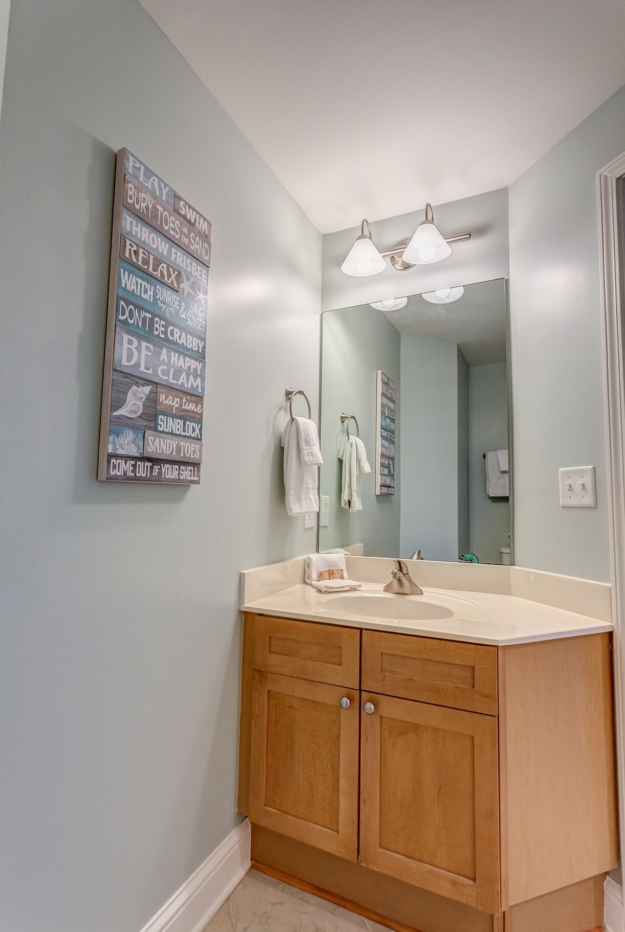 Une salle de bain avec un meuble-lavabo en bois, un grand miroir et un mur décoré d’une citation inspirante.