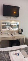 Una habitación de hotel con cama, escritorio con espejo, televisión y tetera.