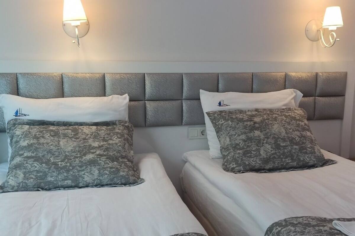 A hotel room with two beds, each with a headboard and pillows. There are wall-mounted lights above the beds.