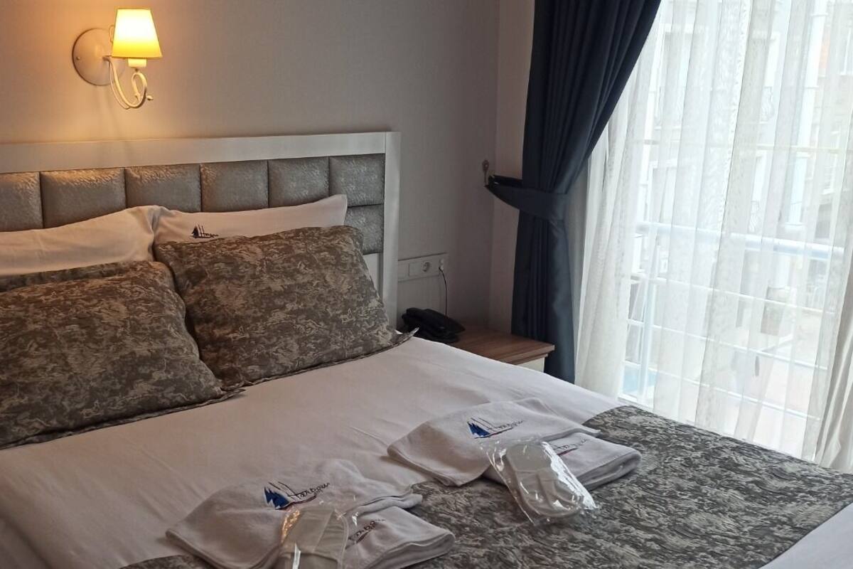 A hotel room with a bed, pillows, a nightstand, a lamp, and a window with curtains.