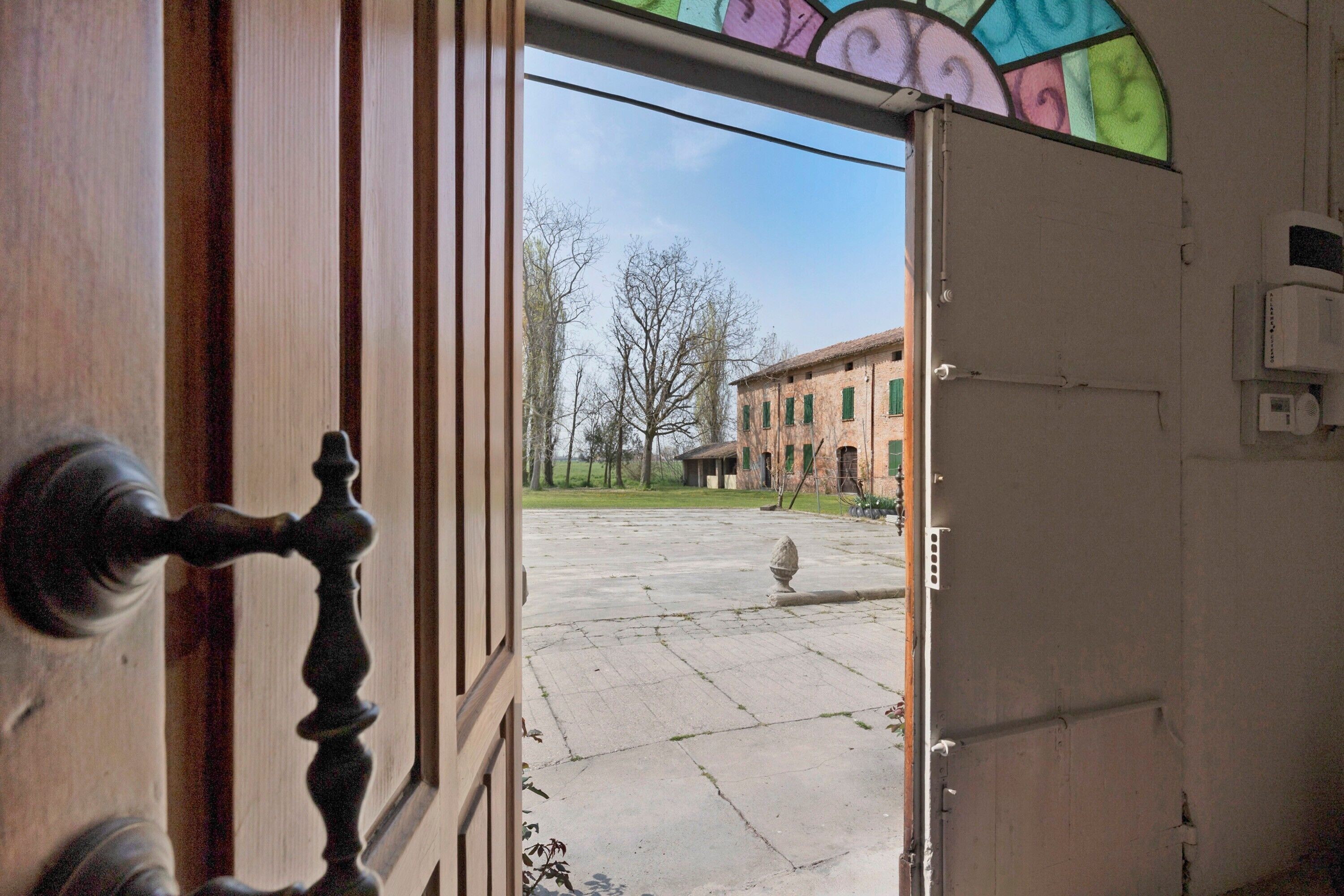 Eine offene Tür mit Blick auf einen Innenhof, ein Gebäude mit grünen Fensterläden und ein klarer Himmel.