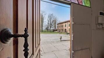 Eine offene Tür mit Blick auf einen Innenhof, ein Gebäude mit grünen Fensterläden und ein klarer Himmel.