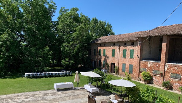 Eine Terrasse im Freien mit Tischen und Stühlen, ein Ziegelgebäude mit grünen Fensterläden und eine Rasenfläche.