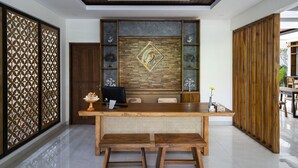 A reception desk with a wooden finish, a modern chandelier, and a decorative wall panel. - The Calna Villa (Kuta)