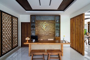 A reception desk with a wooden finish, a modern chandelier, and a decorative wall panel. - The Calna Villa (Kuta)