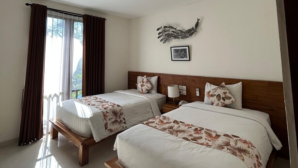 A hotel room with two beds, a wooden headboard, a wall-mounted air conditioner, and a window with curtains. - The Calna Villa (Kuta)