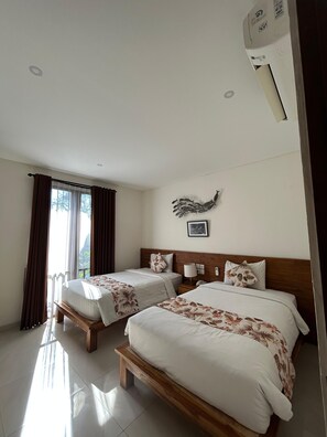 A hotel room with two beds, a wooden headboard, a wall-mounted air conditioner, and a window with curtains. - The Calna Villa (Kuta)