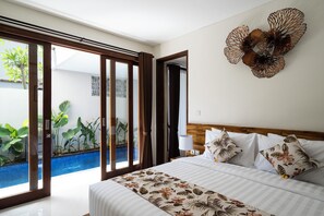 A hotel room with a bed, a view of a swimming pool, and a large decorative wall piece. - The Calna Villa (Kuta)