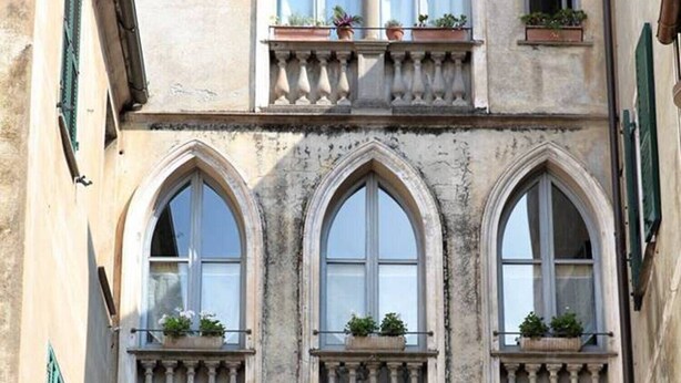 A multi-story building with arched windows, balconies with potted plants, and a decorative garland. - Pet-Friendly Apartment Bilocale Merlino with Mountain View & Wi-Fi (Finale Ligure)