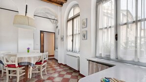 A dining area with a checkered floor, a round table with chairs, a hanging lamp, and a window with curtains. - Pet-Friendly Apartment Bilocale Merlino with Mountain View & Wi-Fi (Finale Ligure)
