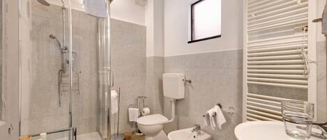 A bathroom with a glass-enclosed shower, a toilet, a bidet, and a sink with a glass container.