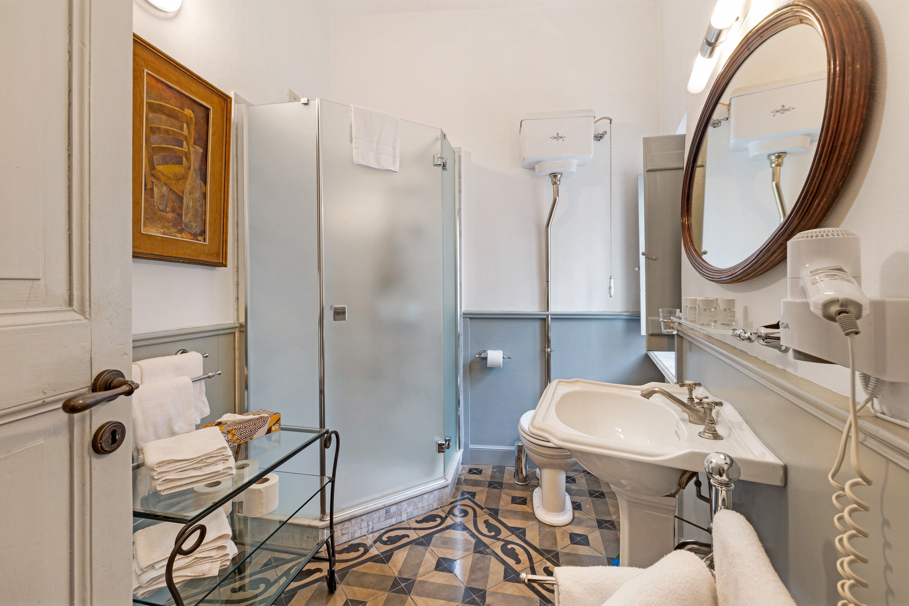 Une salle de bain avec une douche à parois de verre, un lavabo avec un miroir et une étagère en verre où sont posées des serviettes.