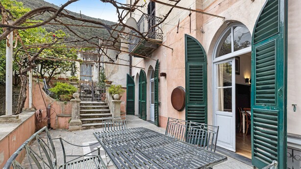 A courtyard with a table and chairs, a staircase, and a door with green shutters. - Pet-Friendly Apartment Quadrilocale Camelot with Mountain View, Balcony & Wi-Fi (Finale Ligure)