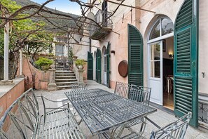 Une cour avec une table et des chaises, un escalier et une porte dotée de volets verts.