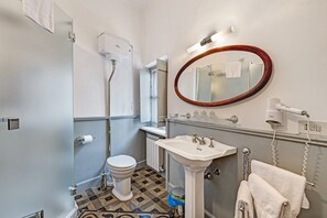 Une salle de bain comprenant des toilettes, un lavabo, un miroir, un porte-serviettes et un espace douche.