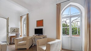 A room with two armchairs, a television on a small table, and a large arched window with curtains. - Pet-Friendly Apartment Quadrilocale Camelot with Mountain View, Balcony & Wi-Fi (Finale Ligure)