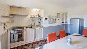 Cozinha equipada com fogão, forno, pia e frigorífico. Há uma mesa de jantar com cadeiras e um objeto decorativo sobre ela.
