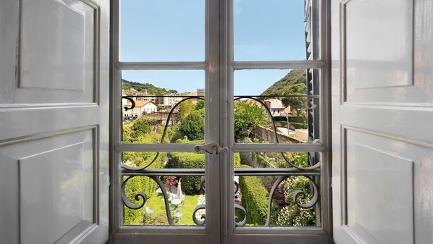 Visão através de uma janela com guarda-corrimão de metal, revelando uma paisagem verde e edifícios ao longe.