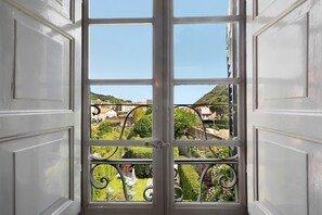 A view through a window with a metal balustrade, revealing a green landscape and buildings in the distance.