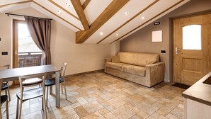 Un espace repas comprenant une table et des chaises, un canapé et un plafond en bois avec des poutres apparentes.