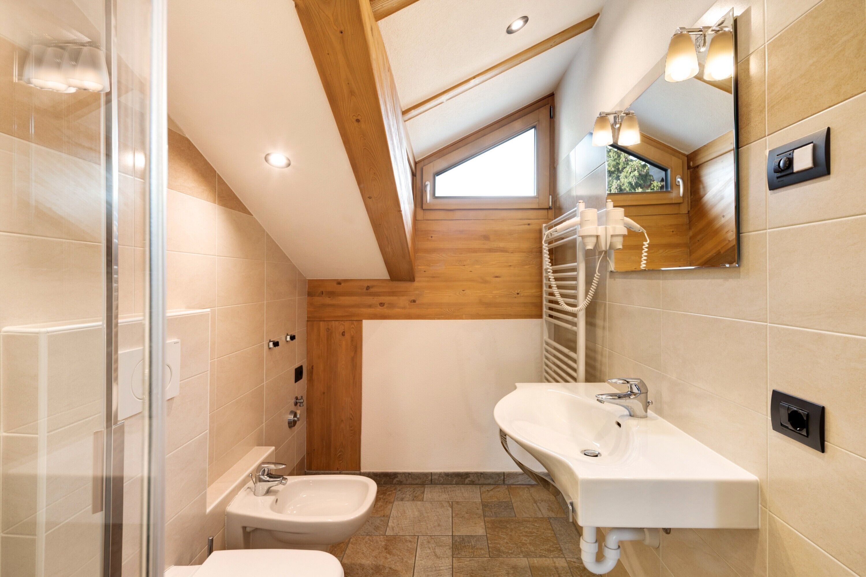 Un baño moderno con ducha, bidé y lavamanos, que presenta vigas de madera y un tragaluz.