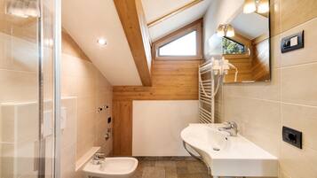 Un baño moderno con ducha, bidé y lavamanos, que presenta vigas de madera y un tragaluz.