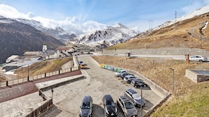 Un parking rempli de voitures, un bâtiment doté d’une tour et, au loin, des montagnes enneigées.
