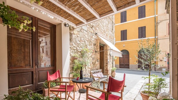 An outdoor seating area with wooden chairs and tables, stone walls, and a yellow building in the background. - Studio "Radicondoli" with Balcony & Wi-Fi (Radicondoli Siena)