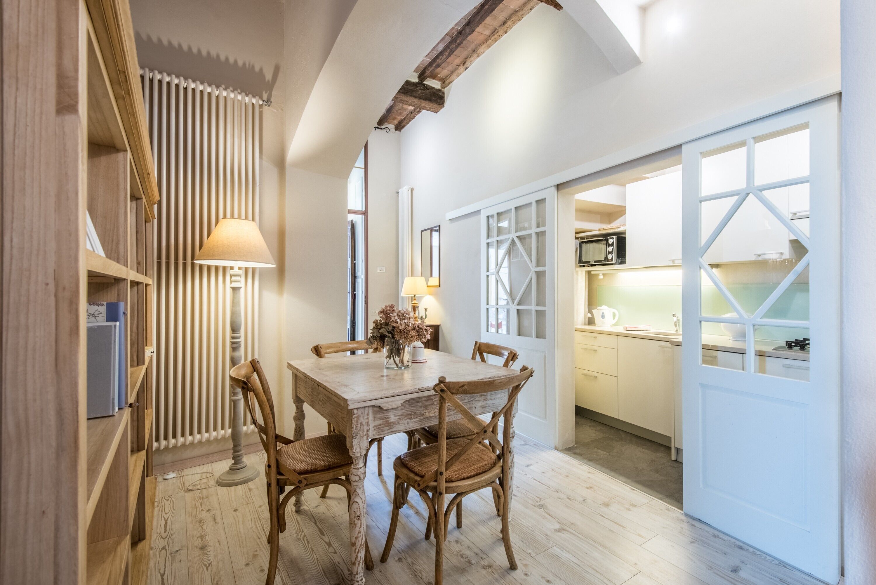 Un comedor con una mesa y sillas de madera, una lámpara y vista a la cocina.