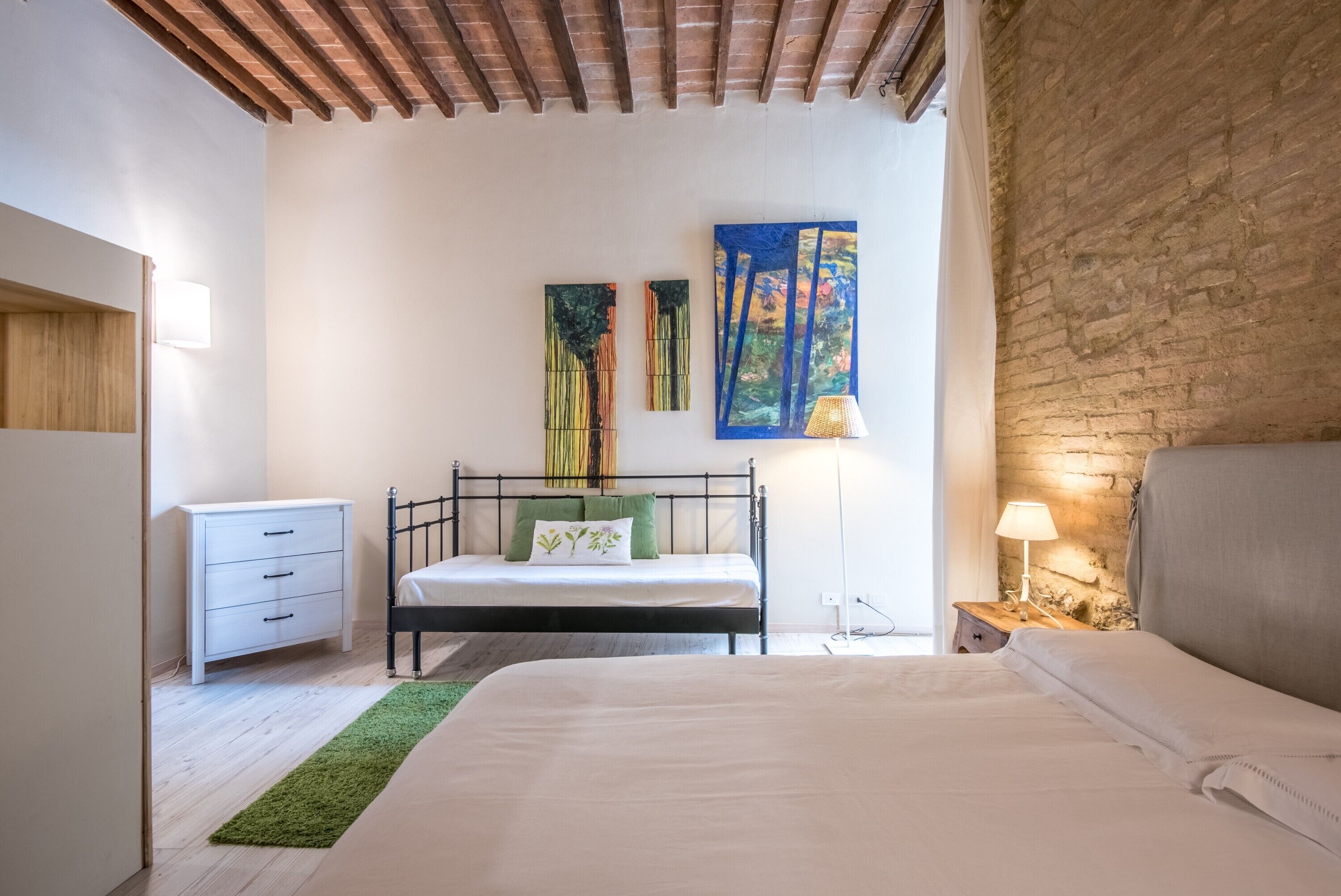A bedroom with a bed, bedside table, lamp, and two paintings on the wall.