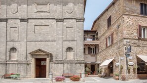 A historic stone building with a central entrance, a balcony on the upper floor, and a small outdoor seating area with tables and chairs. - Studio "Radicondoli" with Balcony & Wi-Fi (Radicondoli Siena)
