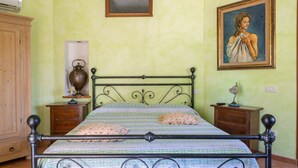 Une chambre à coucher avec un lit, deux tables de chevet, une armoire en bois, un tableau et une fenêtre.