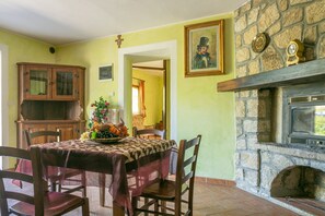A dining area with a stone fireplace, a wooden cabinet, and a table set with a floral centerpiece. - Pet-Friendly Finca 'Flores' with Mountain View, Shared Pool & Wi-Fi (Roccastrada GR)