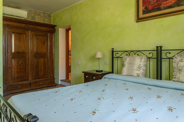 A bedroom with a bed, a nightstand, a lamp, a wardrobe, and a painting on the wall.