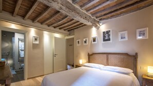 Une chambre avec un plafond en bois, un lit recouvert de draps blancs, une table de chevet avec une lampe et des tableaux encadrés accrochés au mur.