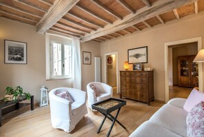 A living room with wooden beams, a white sofa, a white armchair, a wooden cabinet, and a small table with a tray.