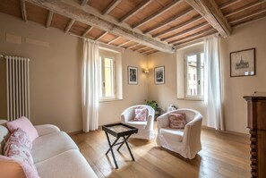 A room with a wooden ceiling, two white armchairs, a small table, and a radiator.