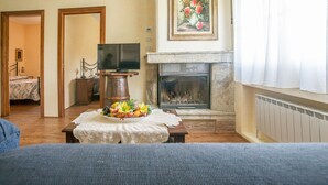 Een woonkamer met een open haard, een televisie en een eettafel met een bloemstuk.