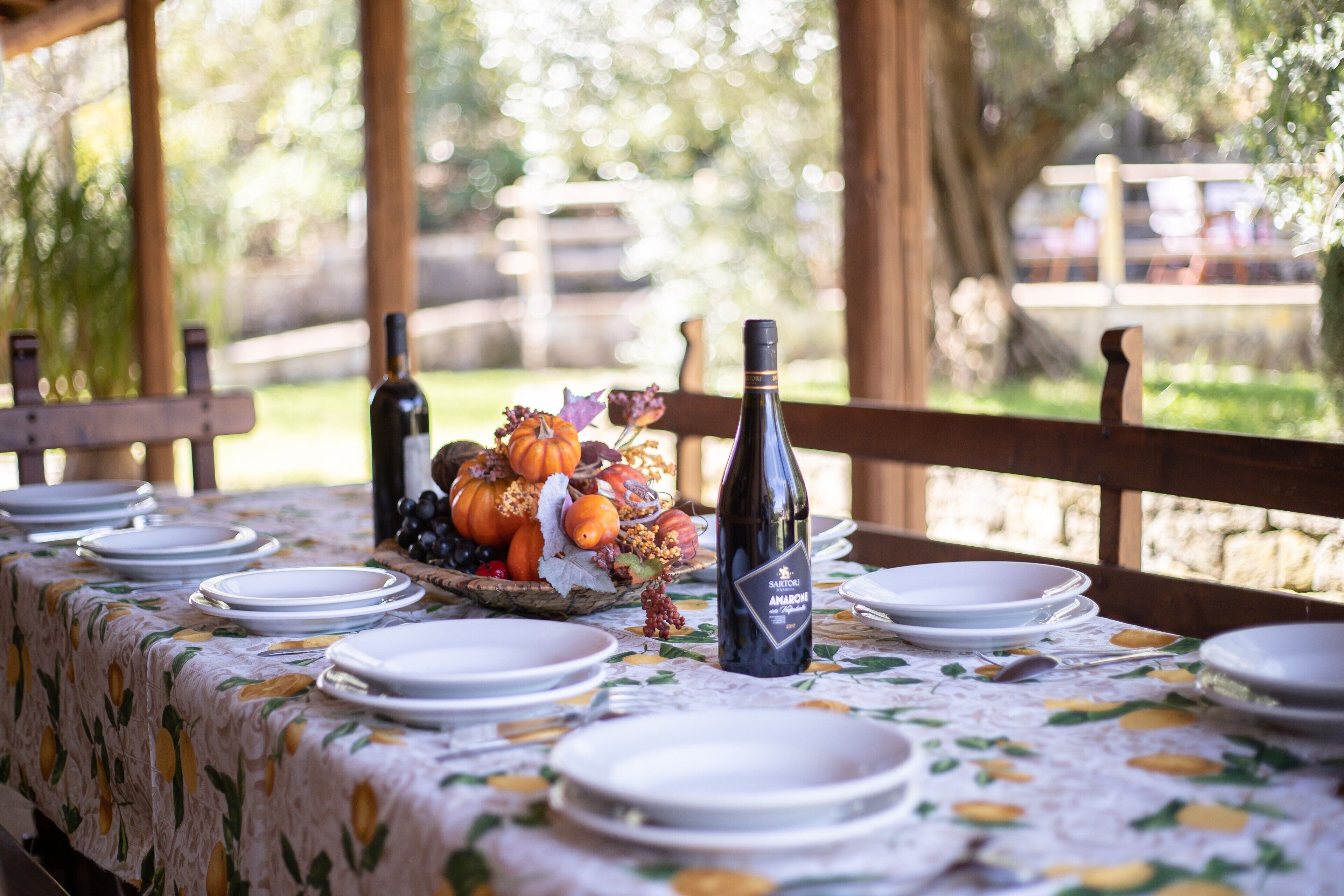A table set outdoors with plates, a bottle of wine, and a fruit arrangement.