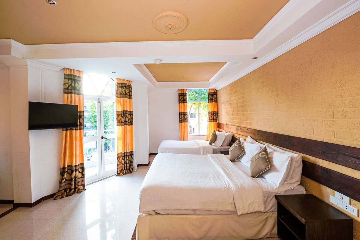 A hotel room with two beds, a flat-screen TV mounted on the wall, and a brick-patterned wall.